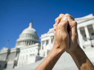 Hands clasped together in front of a capital building. 