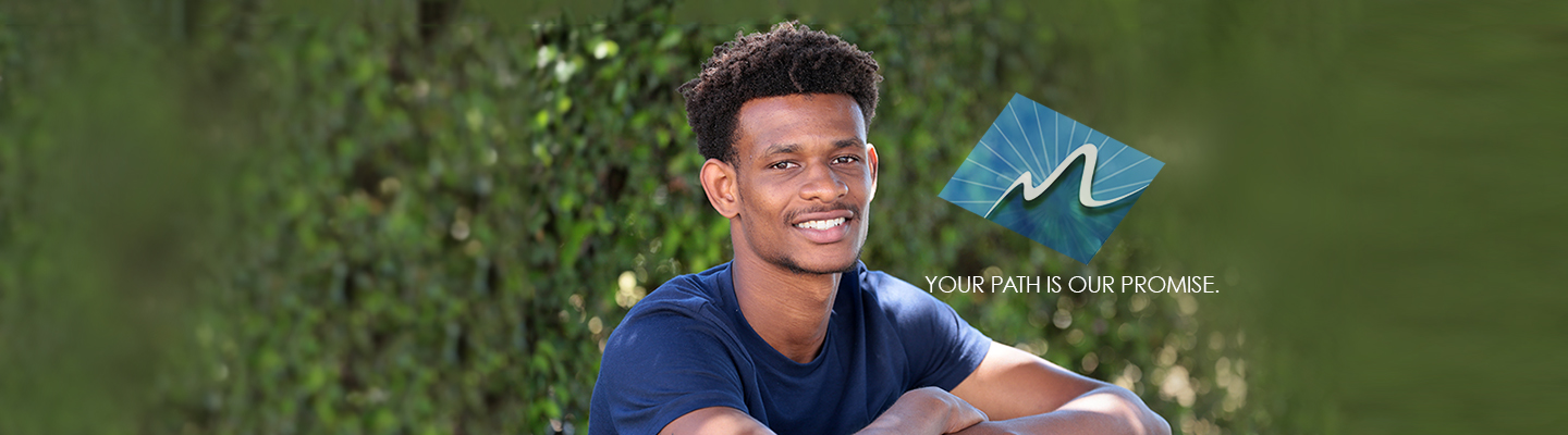 Young black man smiling at you in front of green bushes