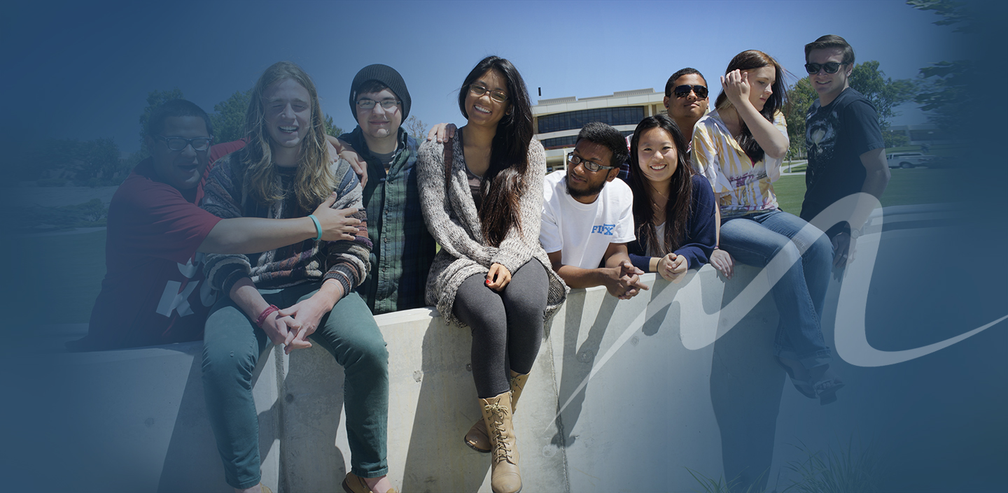 young group of MC students on wall at campus under large M logo