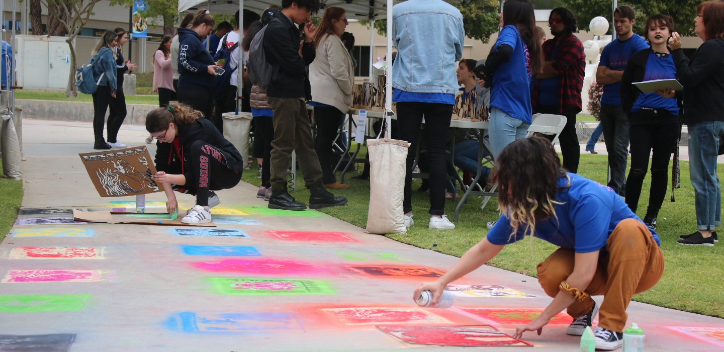 Students spray paint chalk on the sidewalk as part of the 2019 MakerFaire.