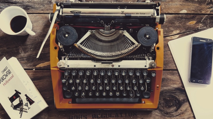 Photo of a typewriter, book, and coffee cup on a desk