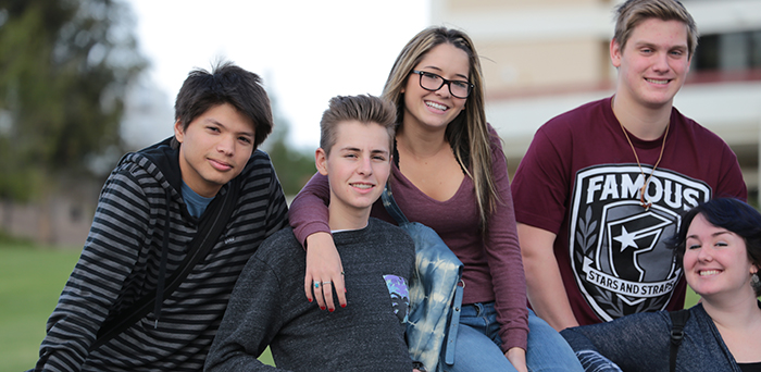 five young adults smiling while sitting on campus wall