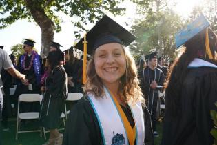 A student smiles for the camera before crossing the stage to receive her diploma. Text below reads: Academic, Academic Programs and Offerings
