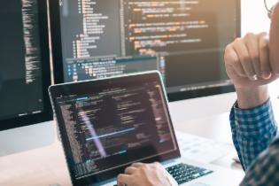A person looking at programming code on several computer screens.