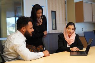 A man and a woman watching a woman demonstrate with a laptop