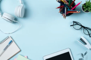 Desk displaying headphones pens tables notebook glasses stapler