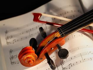 The top of a violin and bow laying across a sheet of music.