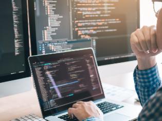 A person looking at programming code on several computer screens.