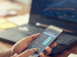 a person using a smart phone and a laptop computer to check financial stocks.