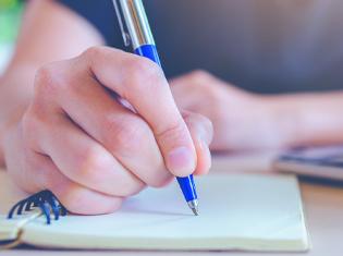 close up of hand with a pen writing on a pad of paper