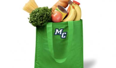 A shopping bag full of produce and groceries. The bag is green and has the athletic "MC" logo on it.