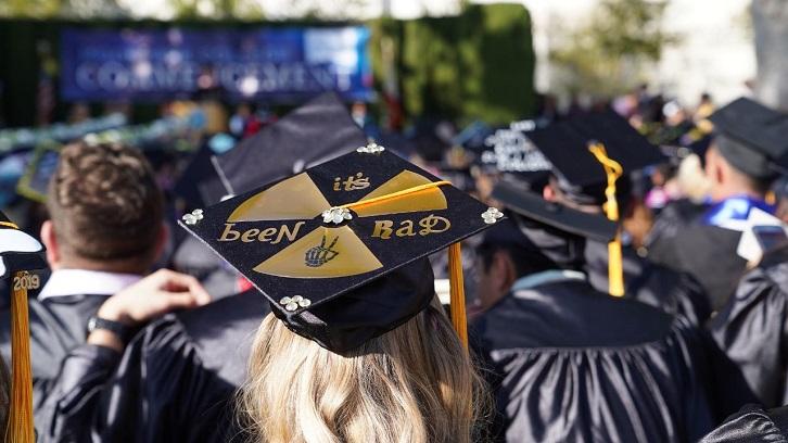 Pictured are graduates from behind, facing the stage where the Commencement ceremony is taking place.