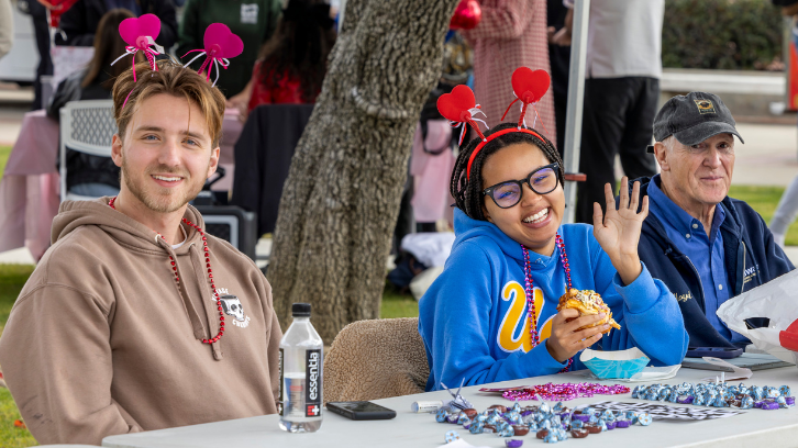 Two students smile at the camera wearing Valentine's Day headbands with hearts on them