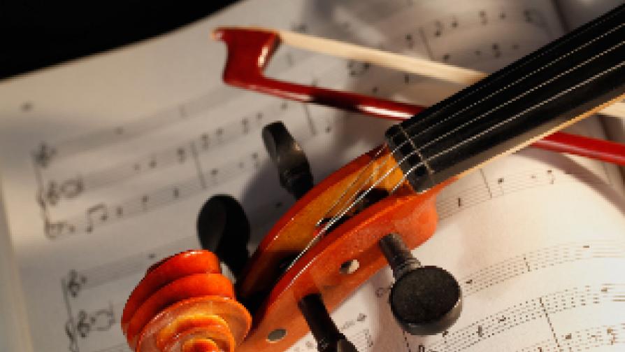 The top of a violin and bow laying across a sheet of music.
