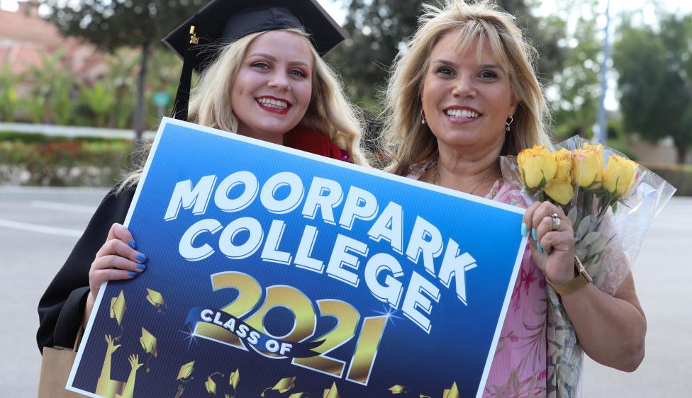Moorpark College Grad with a family member holding up a Class of 2021 sign.