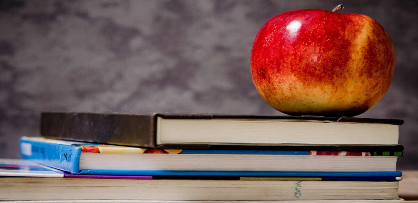 Red apple placed upon the top of a stack of books