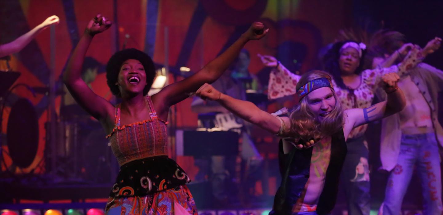 Woman and man sing side by side on stage under purple lights