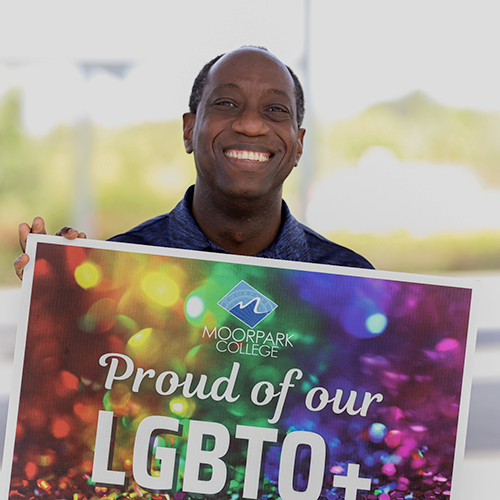 Dr. Sokenu holds up LGBTQ sign